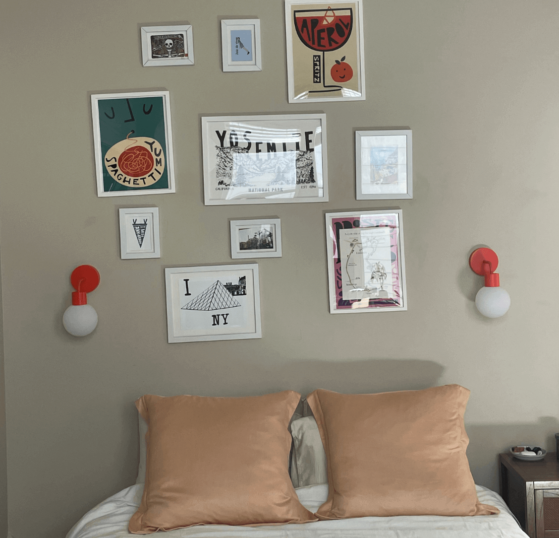 Gallery wall above bed with art frames and red wall sconces, showcasing tool-free sconce hanging technique.