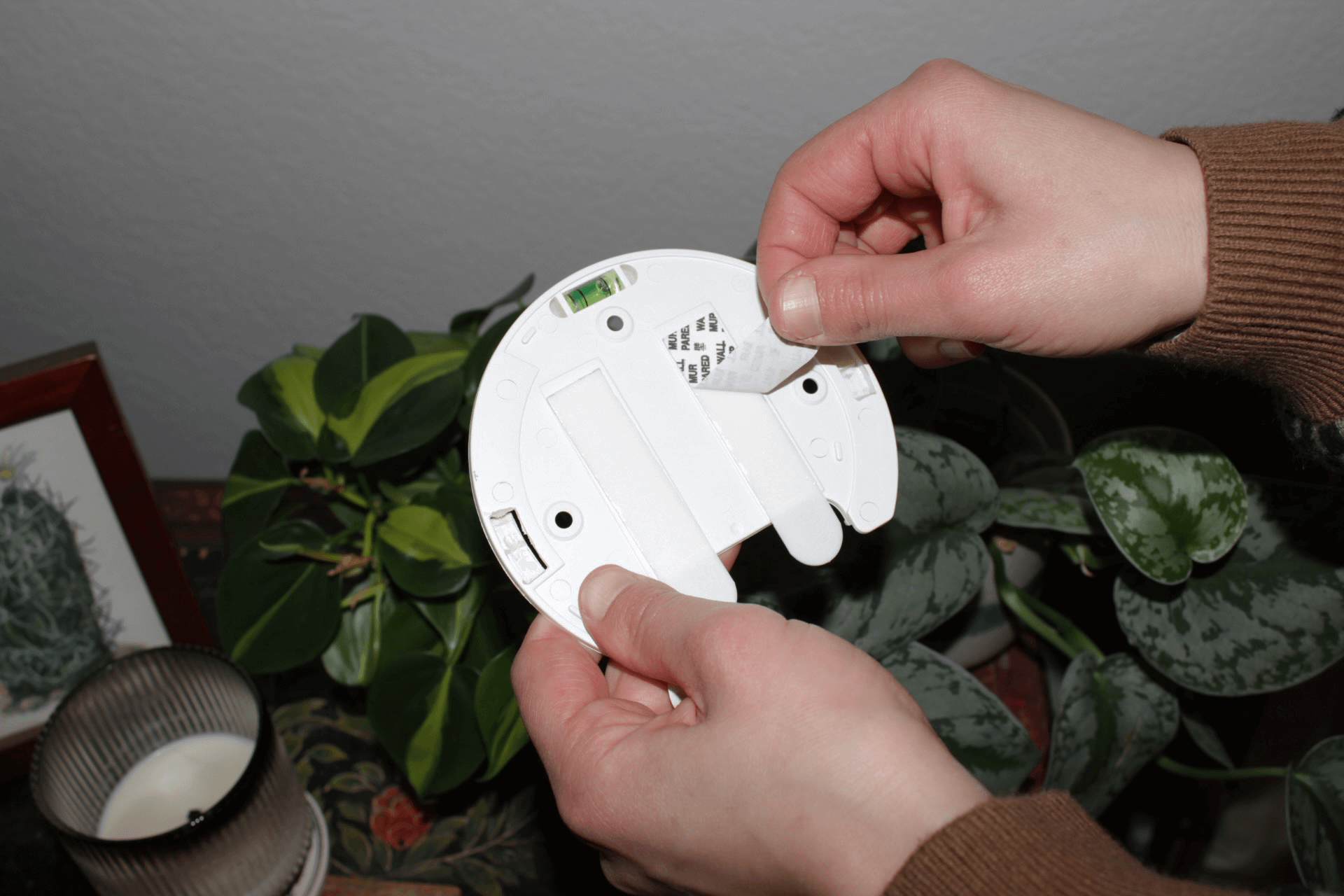 Hands holding a rechargeable wall light base near a potted plant and candle, demonstrating easy installation.