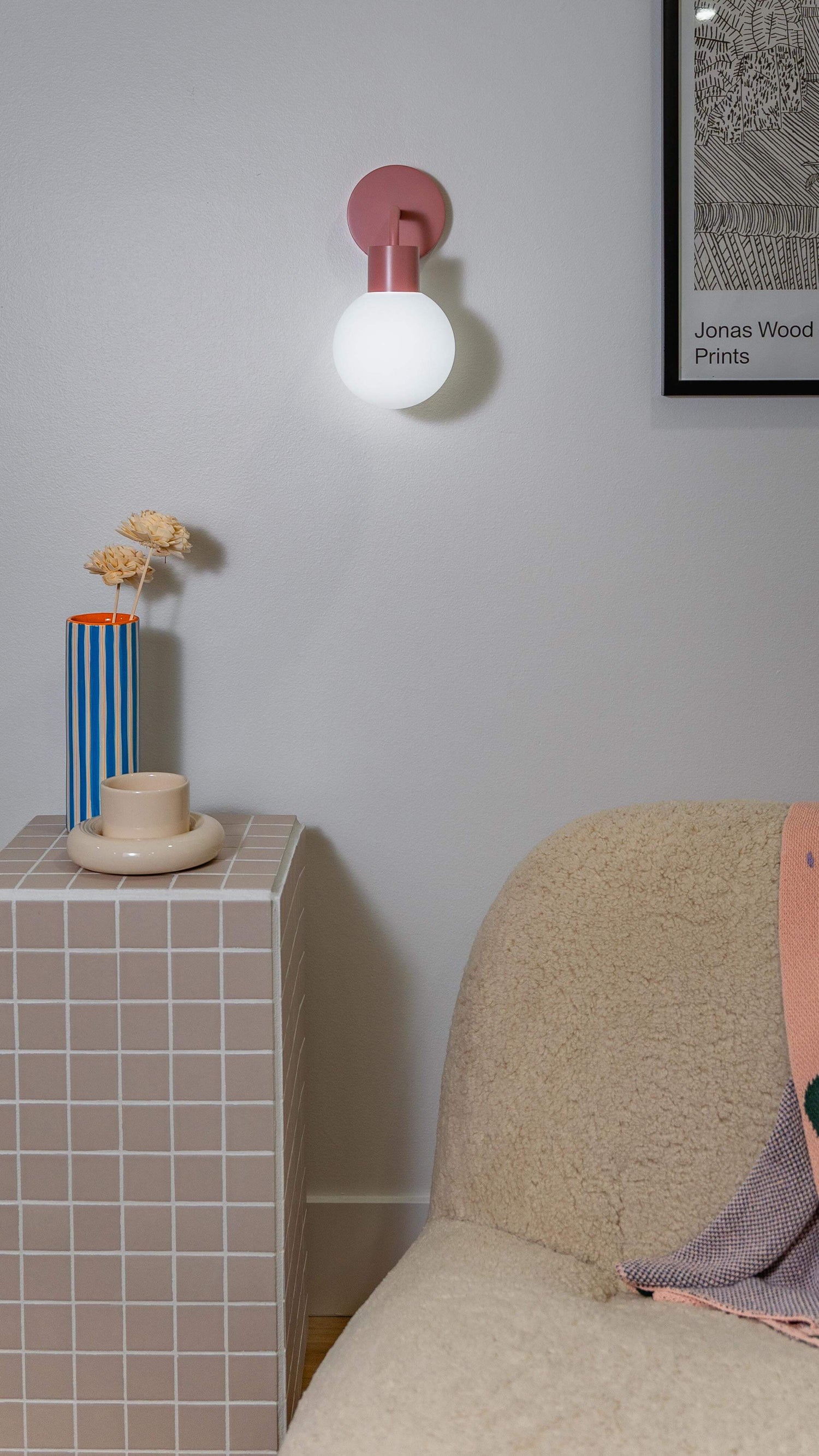 Modern interior with a pink rechargeable wall sconce illuminating a cozy corner, featuring a side table and decorative vase.
