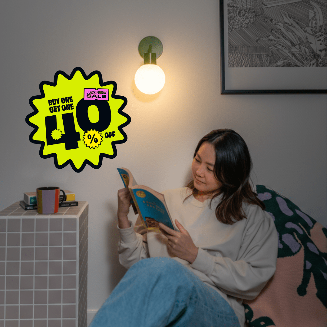 Woman reading a book in a cozy corner illuminated with a Sage Green Poplight wall light sconce and a promotional badge &