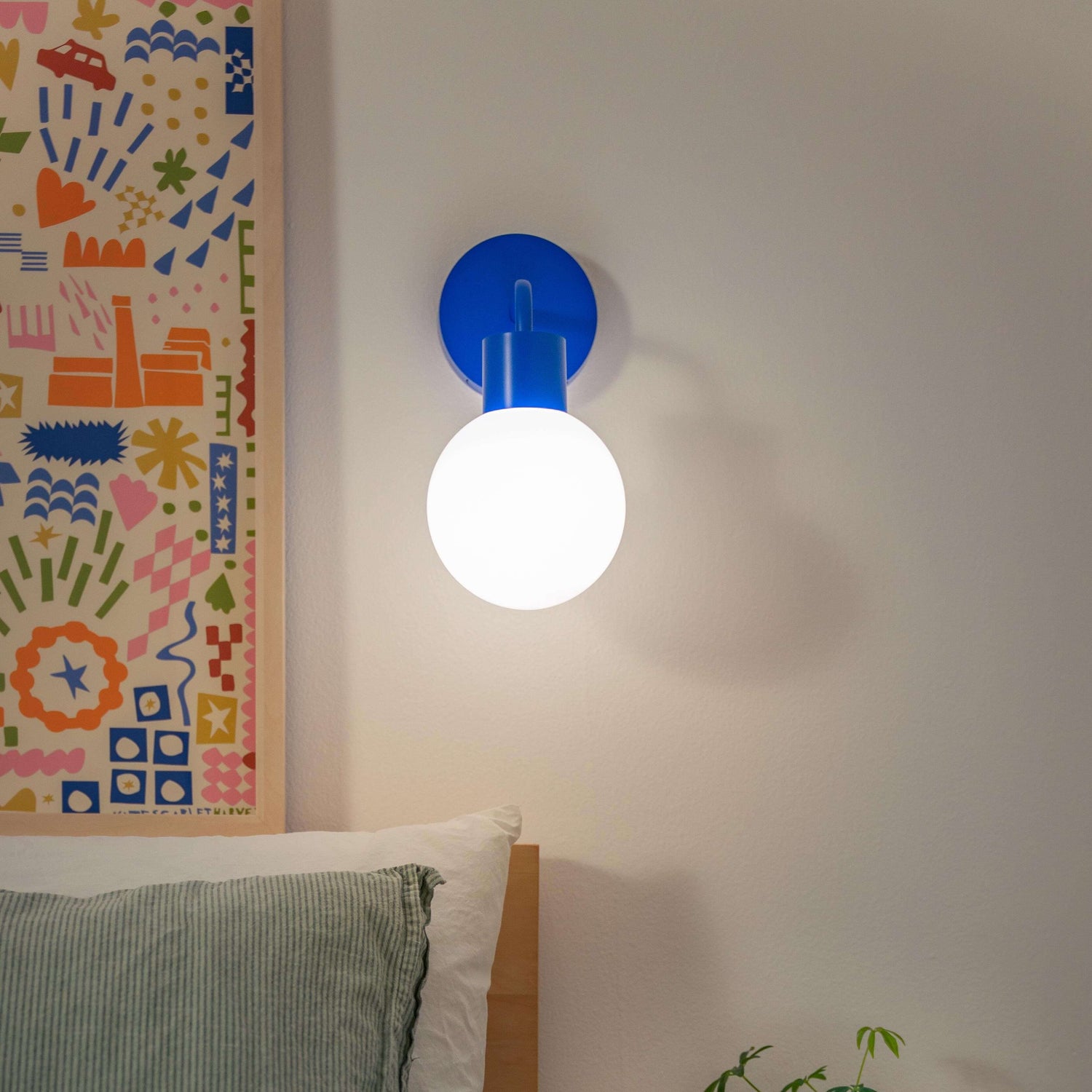 Modern bedroom with a rechargeable wall sconce, featuring a glowing bulb, colorful artwork, and cozy decor.
