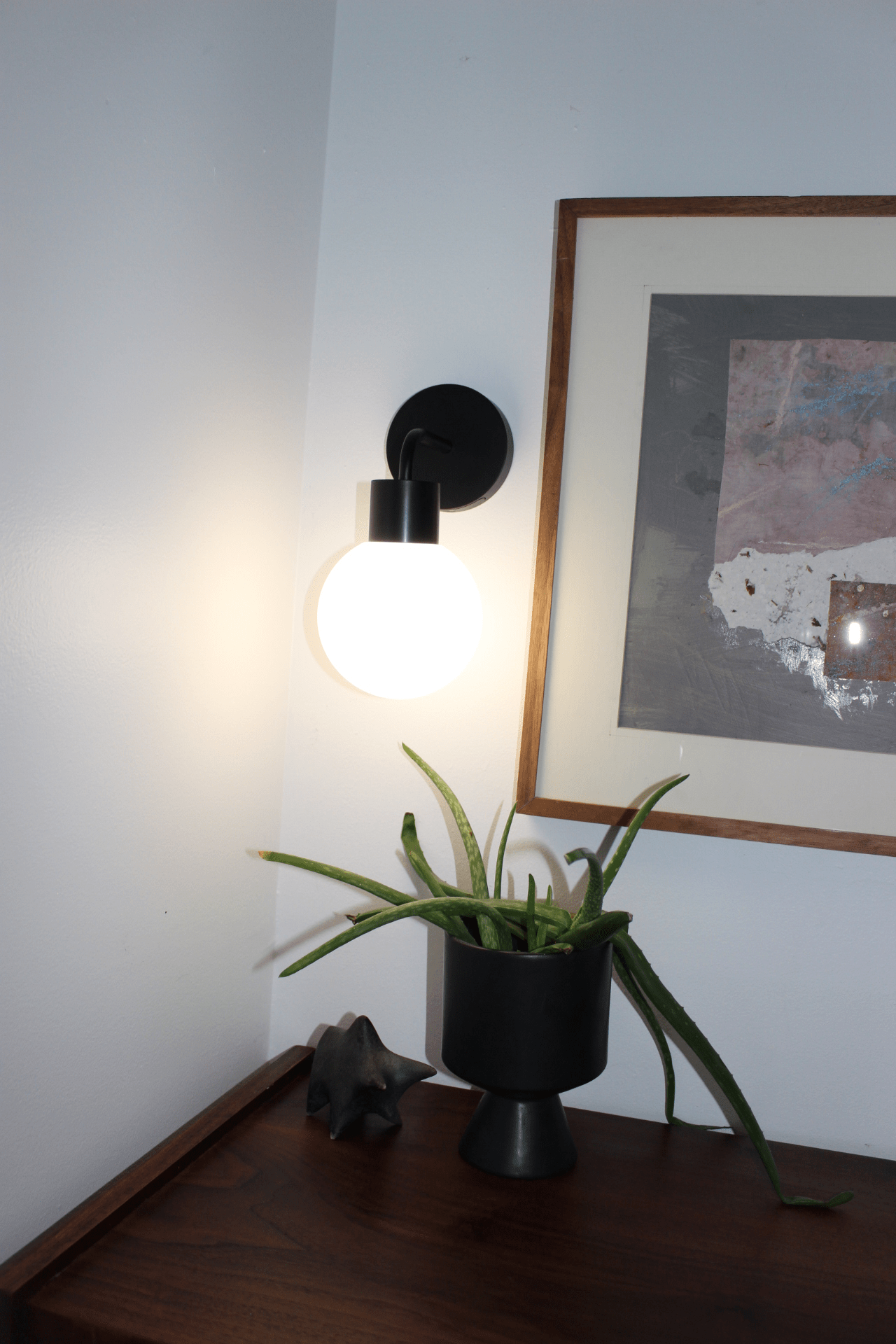 Modern wall lamp illuminating a room, next to a decorative plant in a stylish black pot.