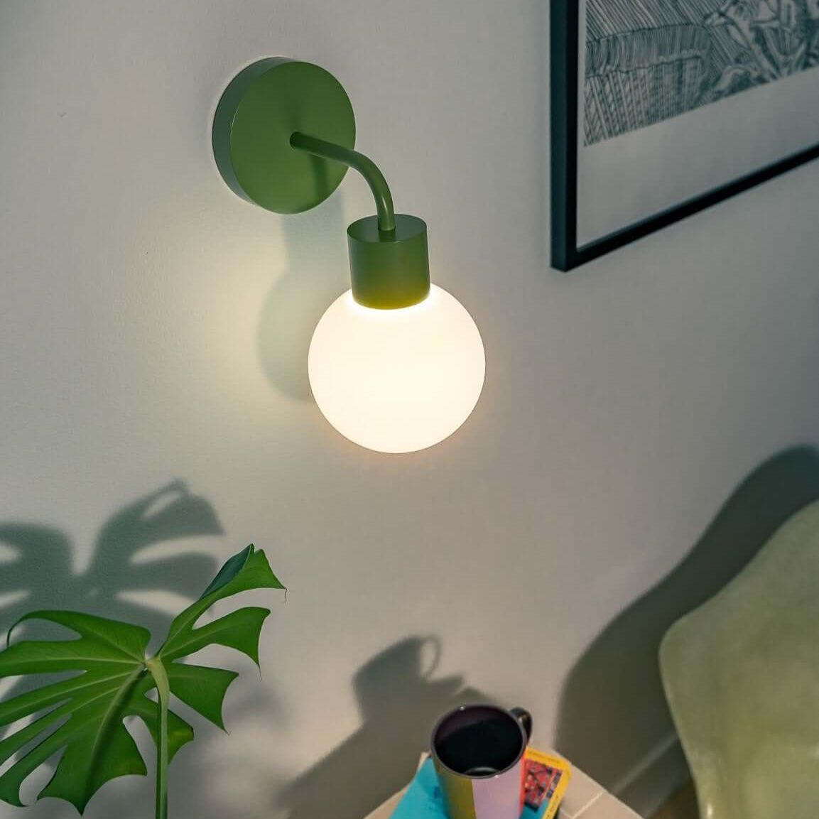 Modern wall lamp illuminating a cozy reading nook with a plant, table, books, and a coffee mug