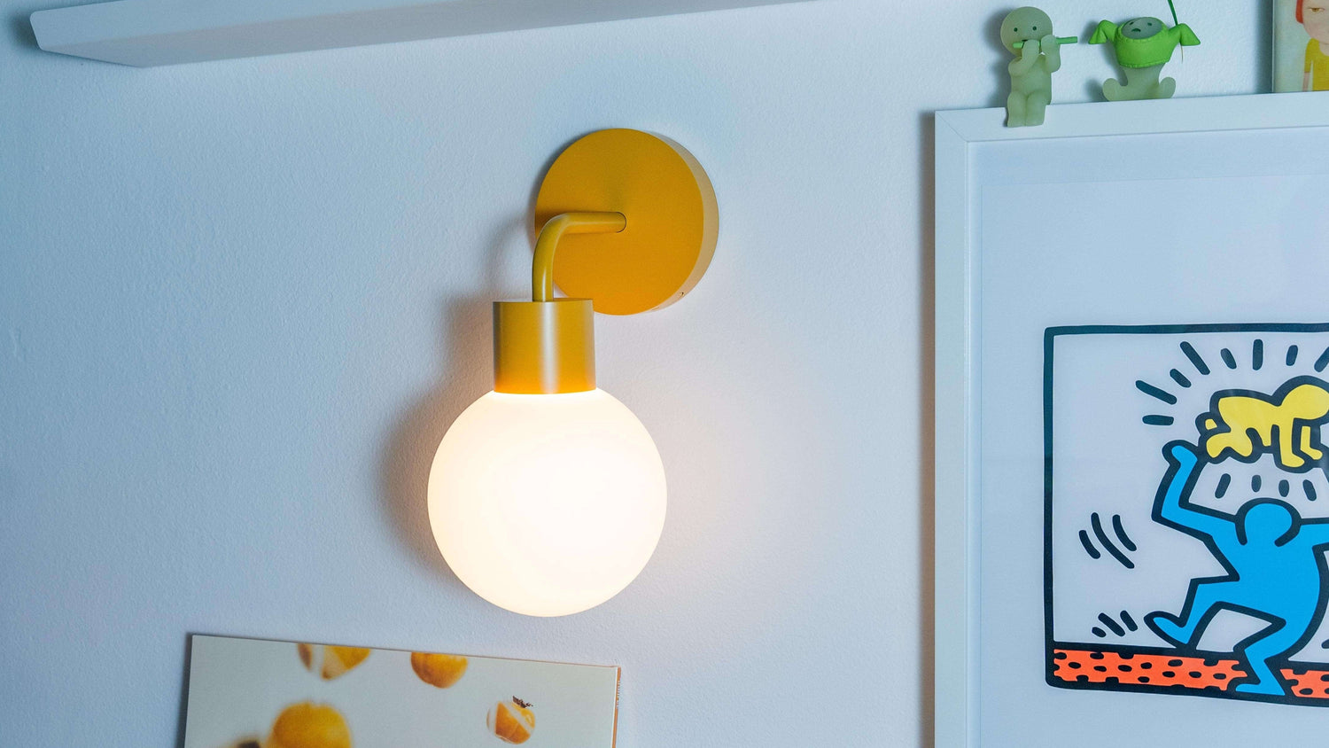 Renter-friendly rechargeable wall sconce illuminating a stylish room decor with art and plants against a white wall.