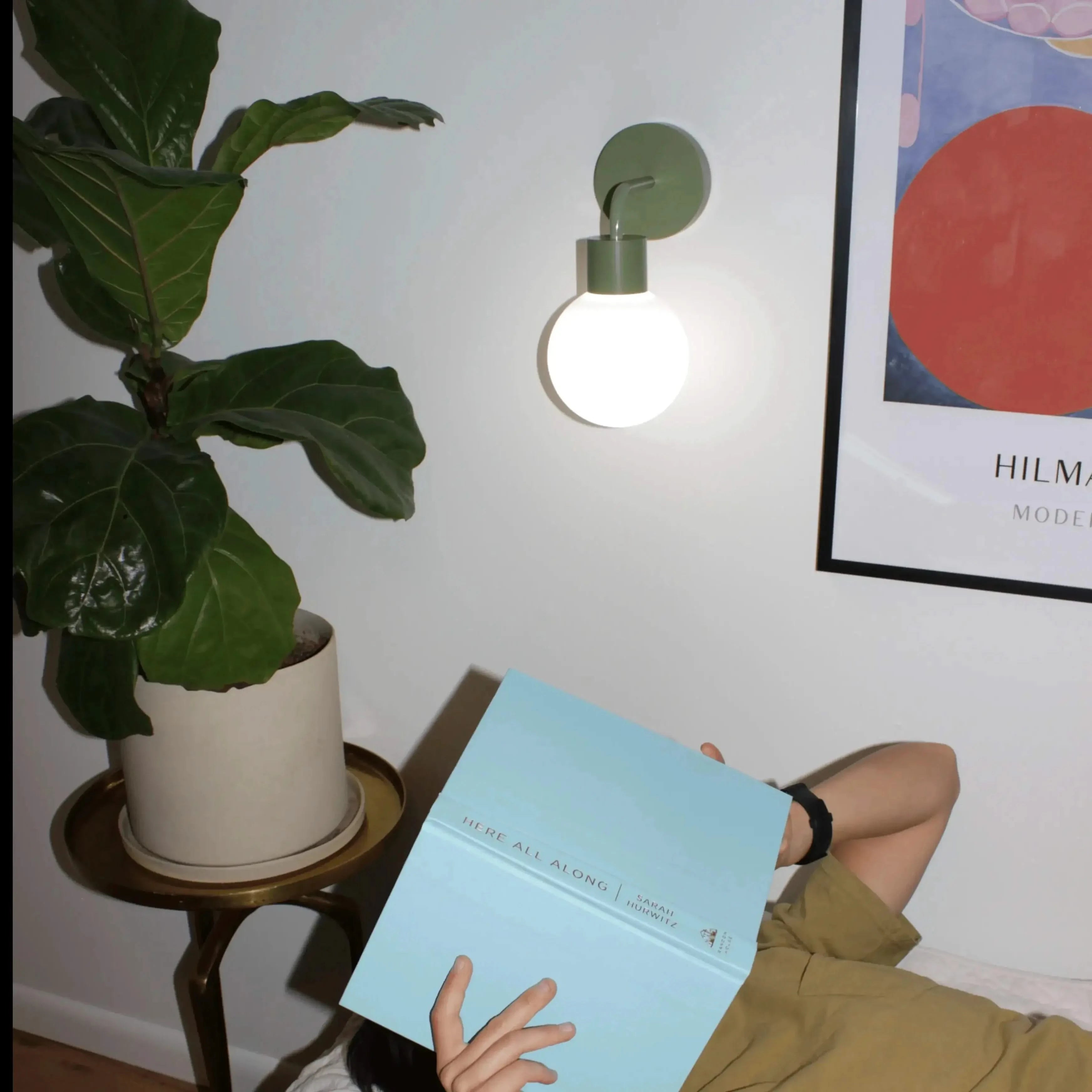 Reading nook illuminated by a sage green rechargeable wall light sconce