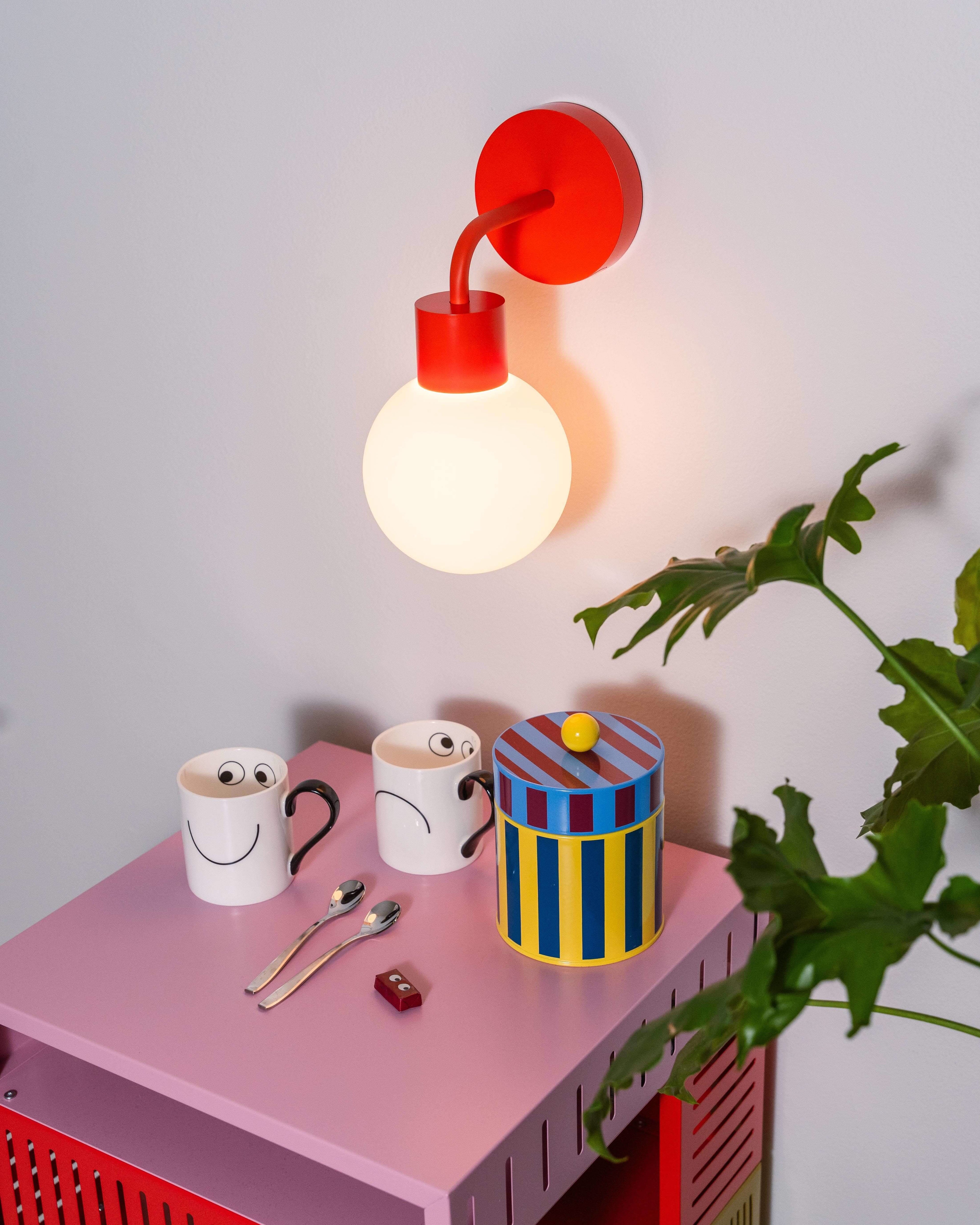 Renter-friendly rechargeable wall sconce with a modern design, illuminating a pink table with decorative mugs and a colorful container.