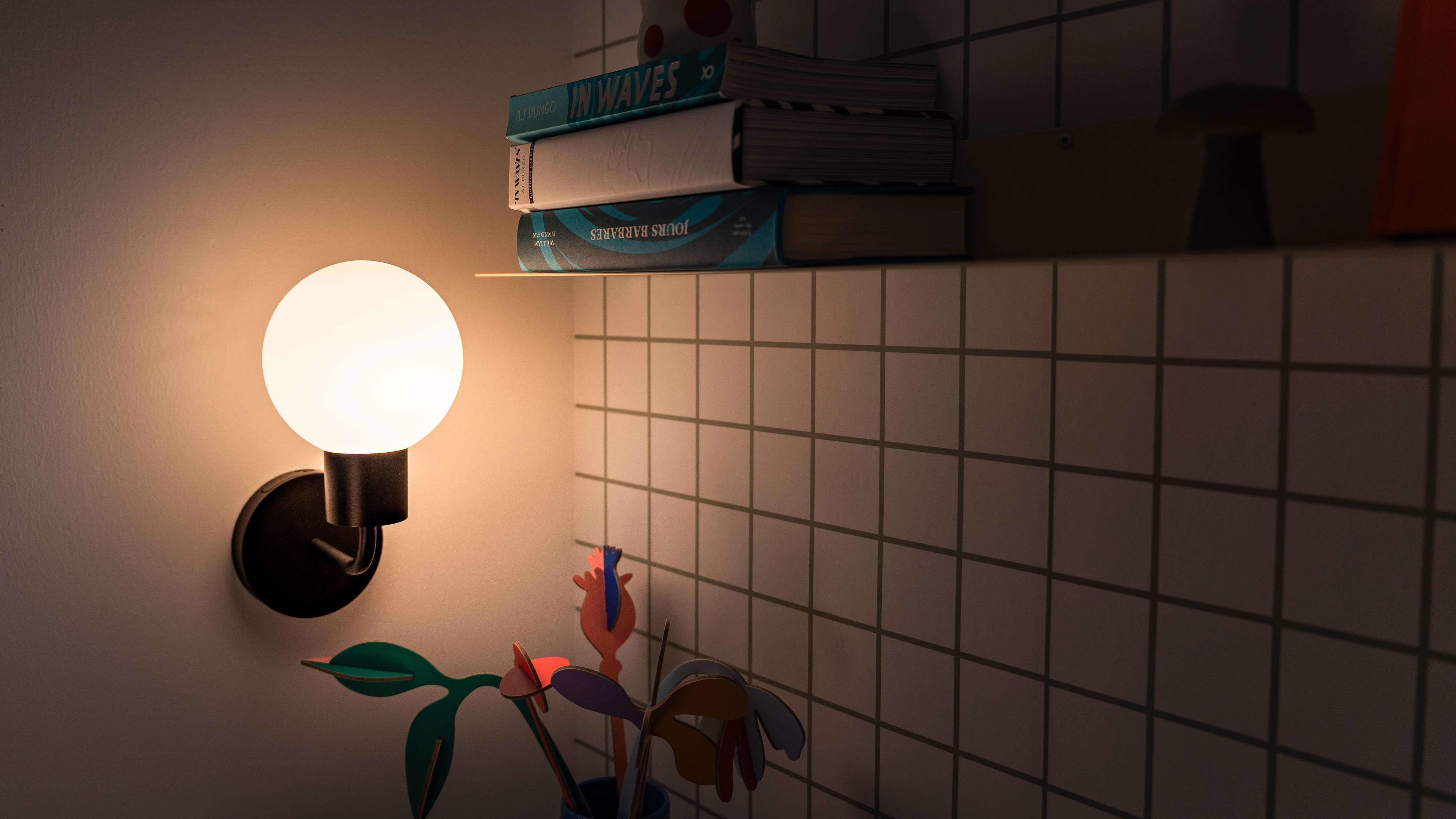 Modern rechargeable wall sconce illuminating a cozy interior with books and decorations on the shelf.
