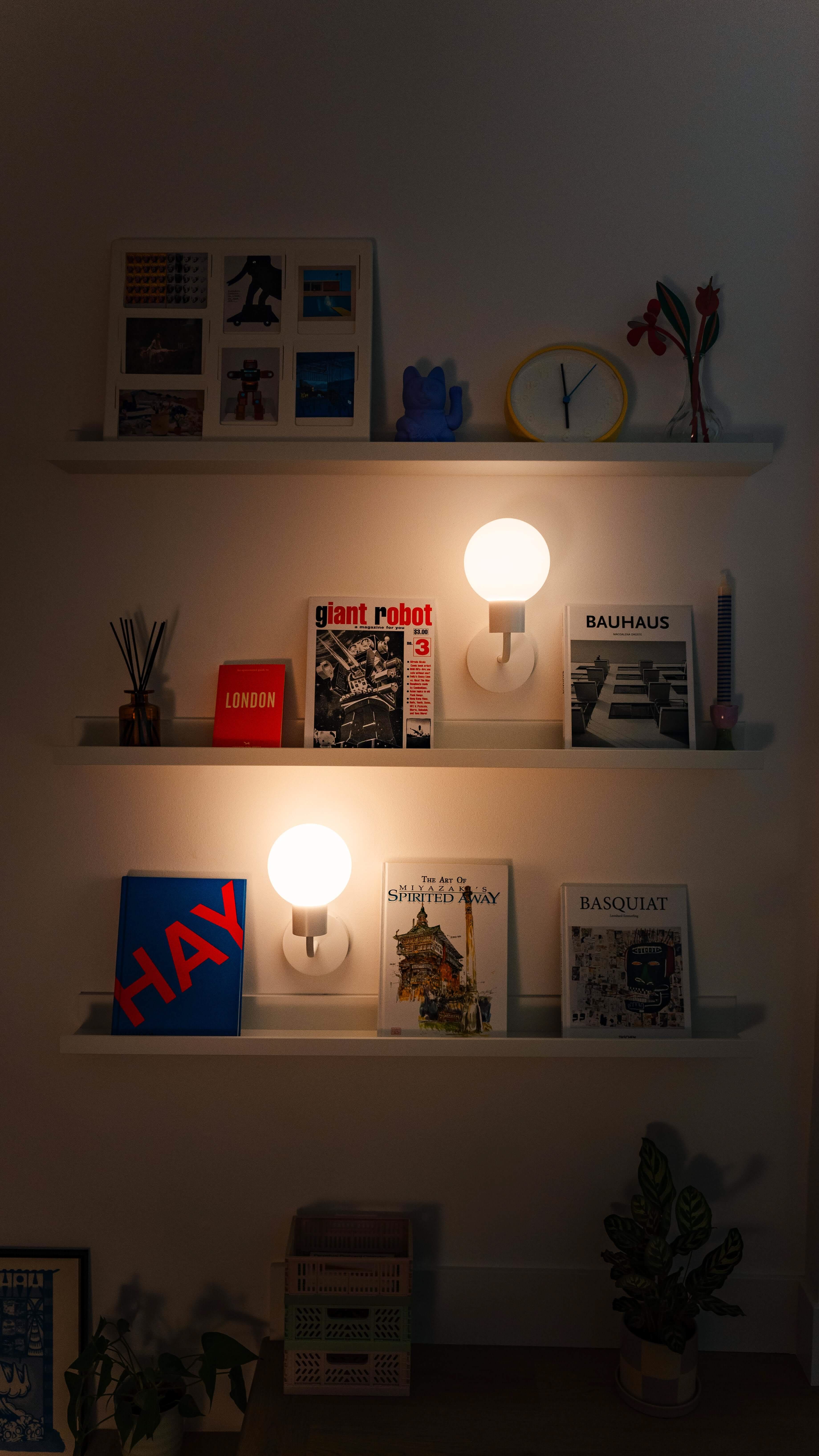 Two rechargeable wall sconces illuminating shelves with books and decor items