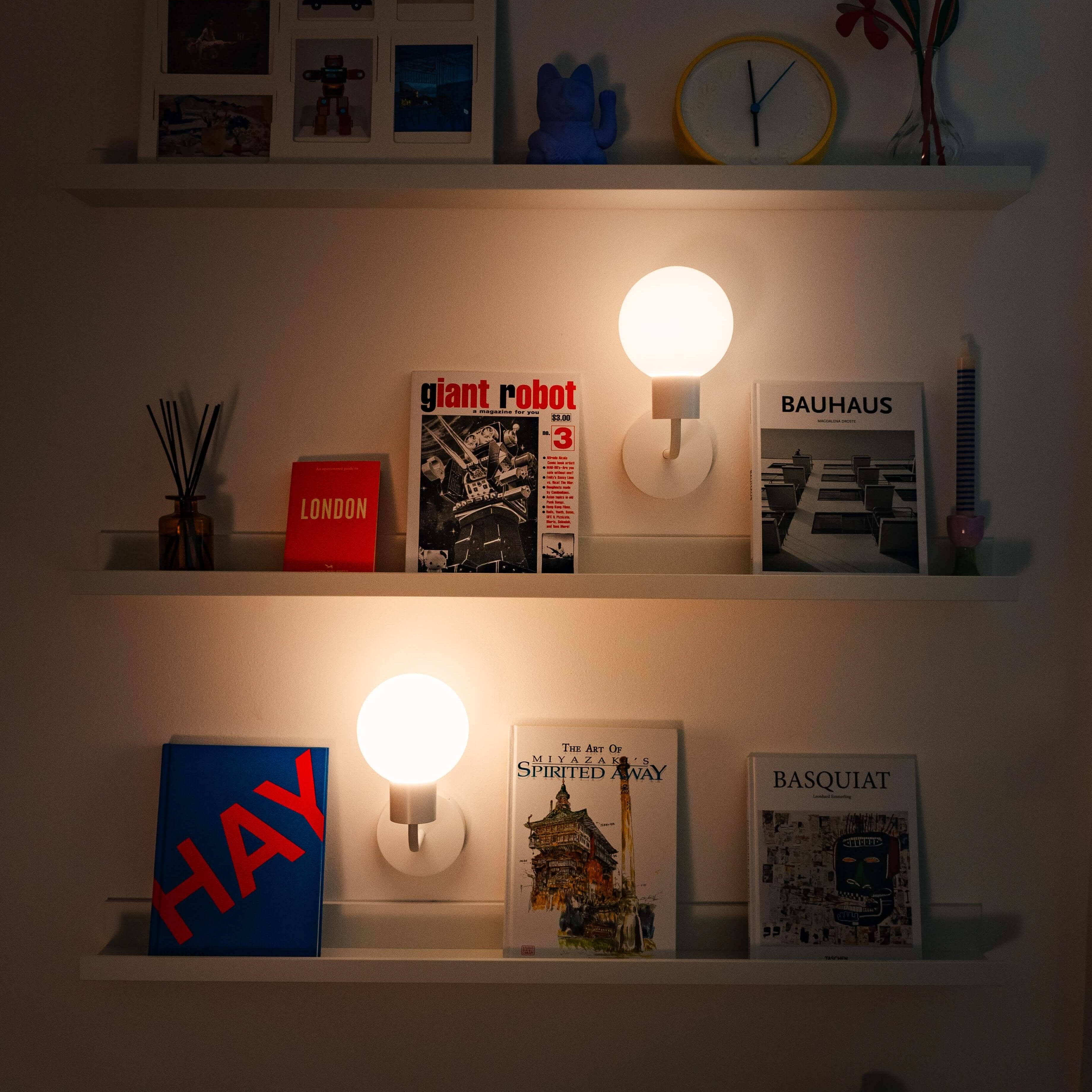 Two rechargeable wall sconces illuminating shelves with books and decor items