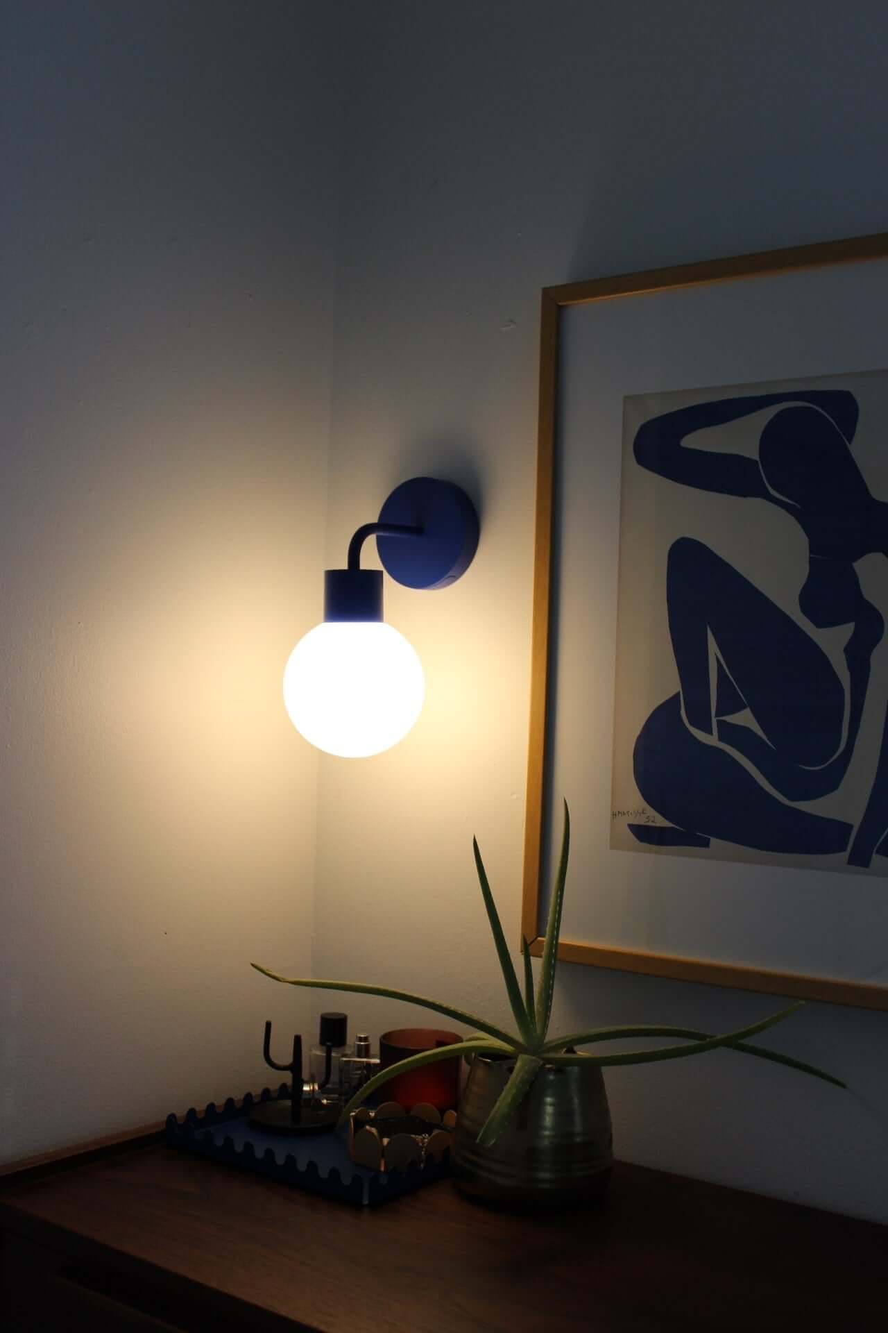 Modern cordless wall sconce illuminating a room, next to framed minimalist artwork and decorative plant for stylish ambiance.