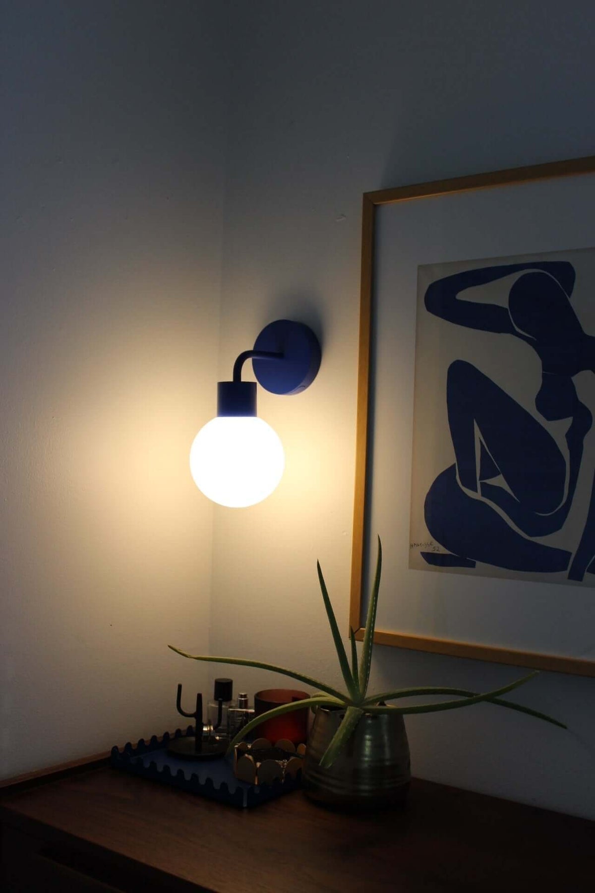 Modern cordless wall sconce illuminating a room, next to framed minimalist artwork and decorative plant for stylish ambiance.