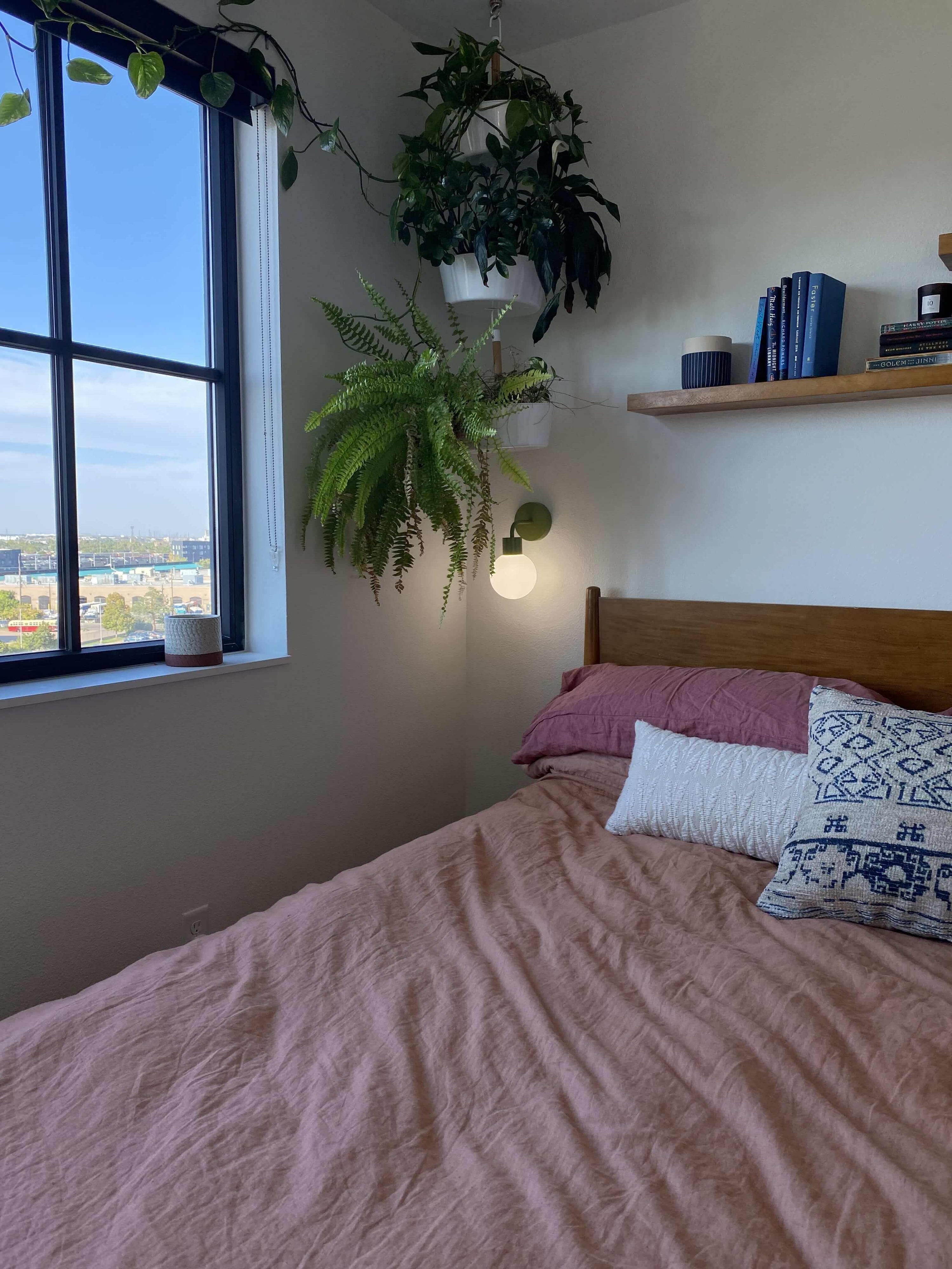 Modern bedroom with pink bedsheet, indoor plants and a Poplight rechargeable wall light sconce