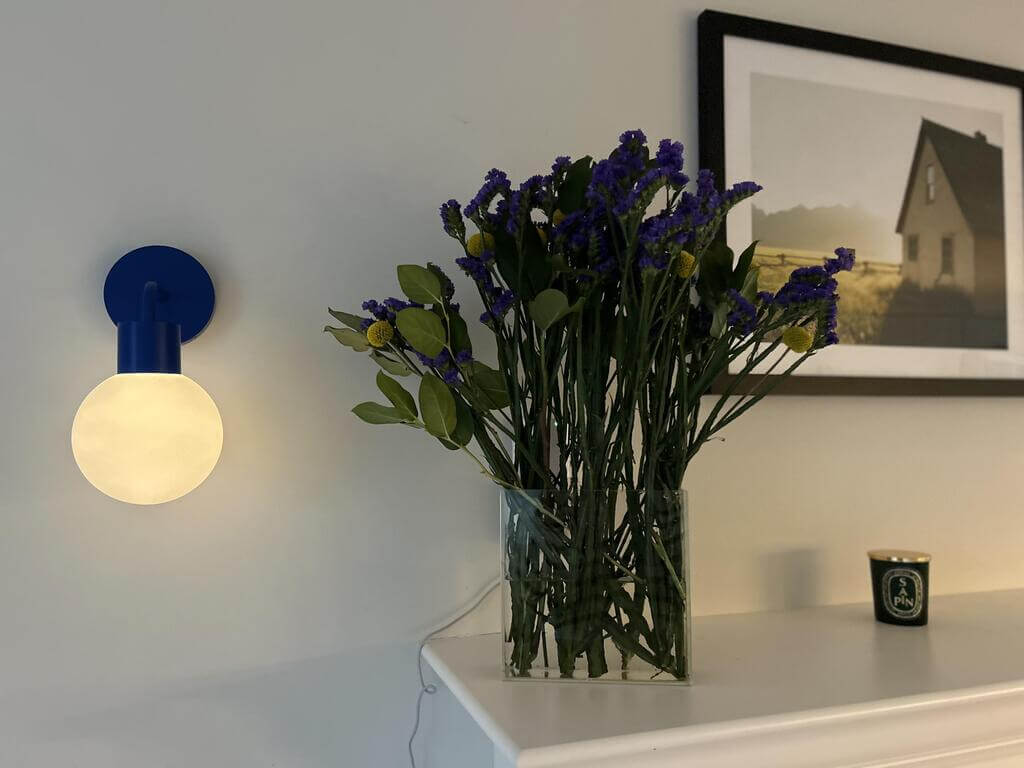 Warm light from blue Poplight rechargeable sconce with a flower vase