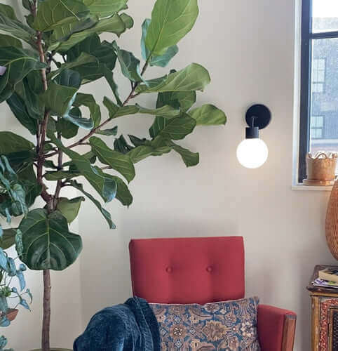 Matte black rechargeable wall light sconce installed in a small corner with a red armchair and an indoor plant