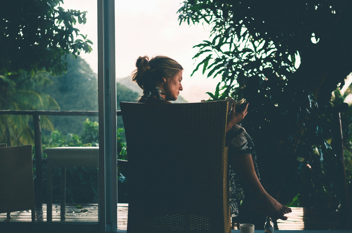A woman comfortably reading a book in a corner while holding a cup of coffee