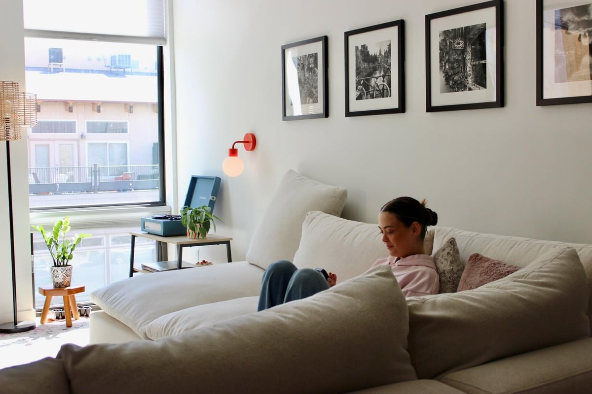 A woman reading while comfortably sitting in a couch in a modern living room accentuated with a wall frames and a rechargeable wall light sconce.