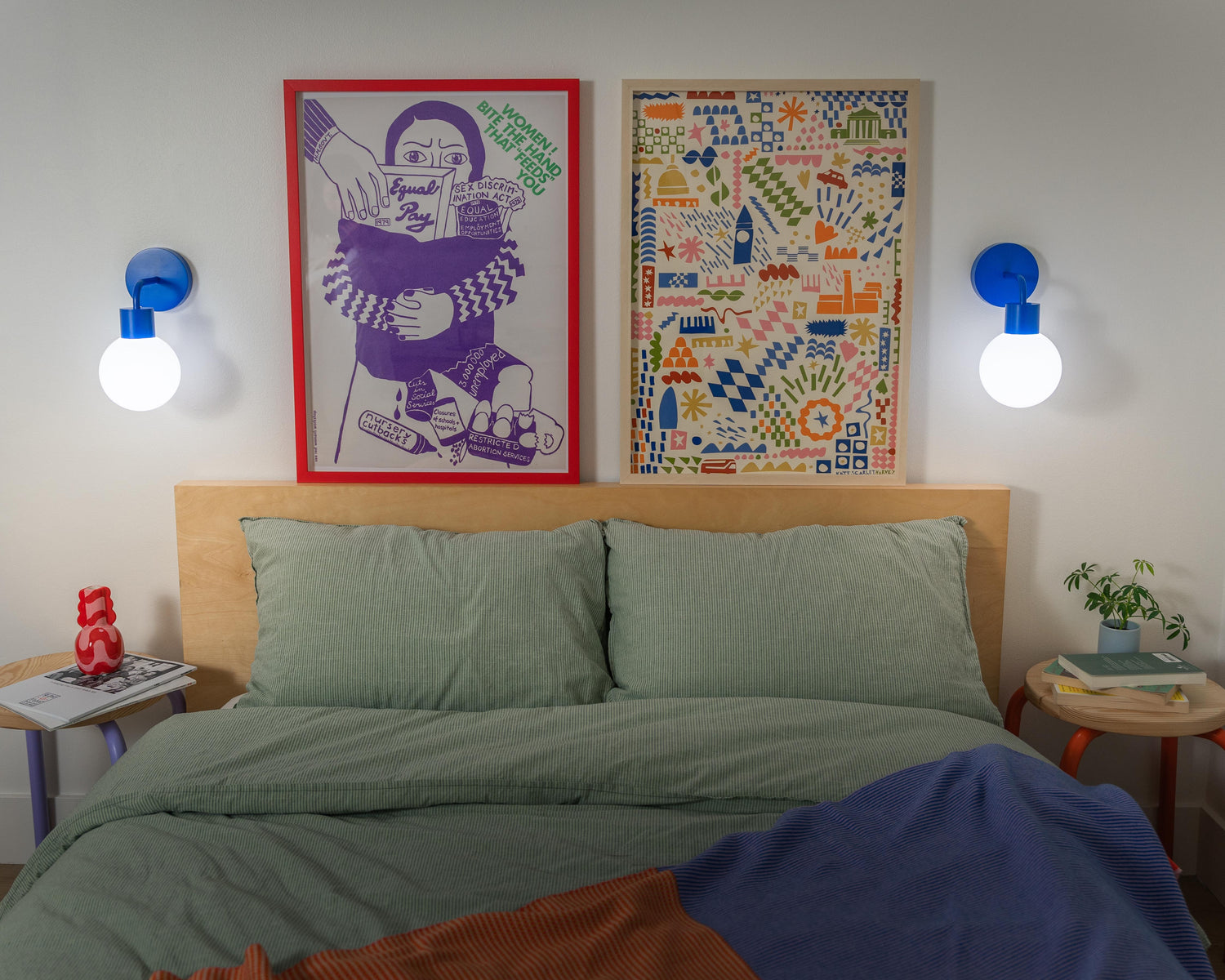 Bedroom with two blue rechargeable wall sconces illuminating modern art above a cozy bed.