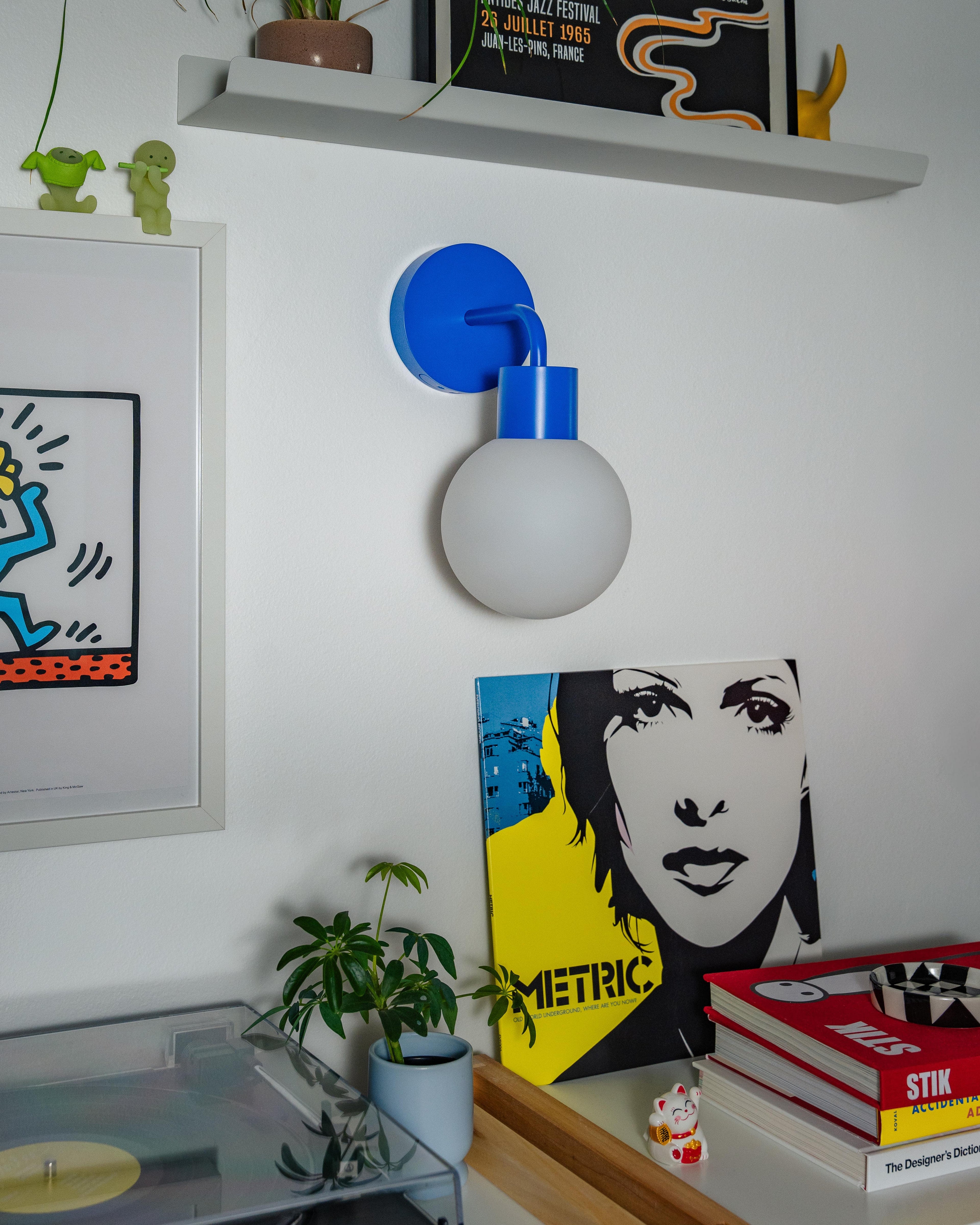 Stylish blue rechargeable wall sconce illuminating a modern room with art and vinyl records.