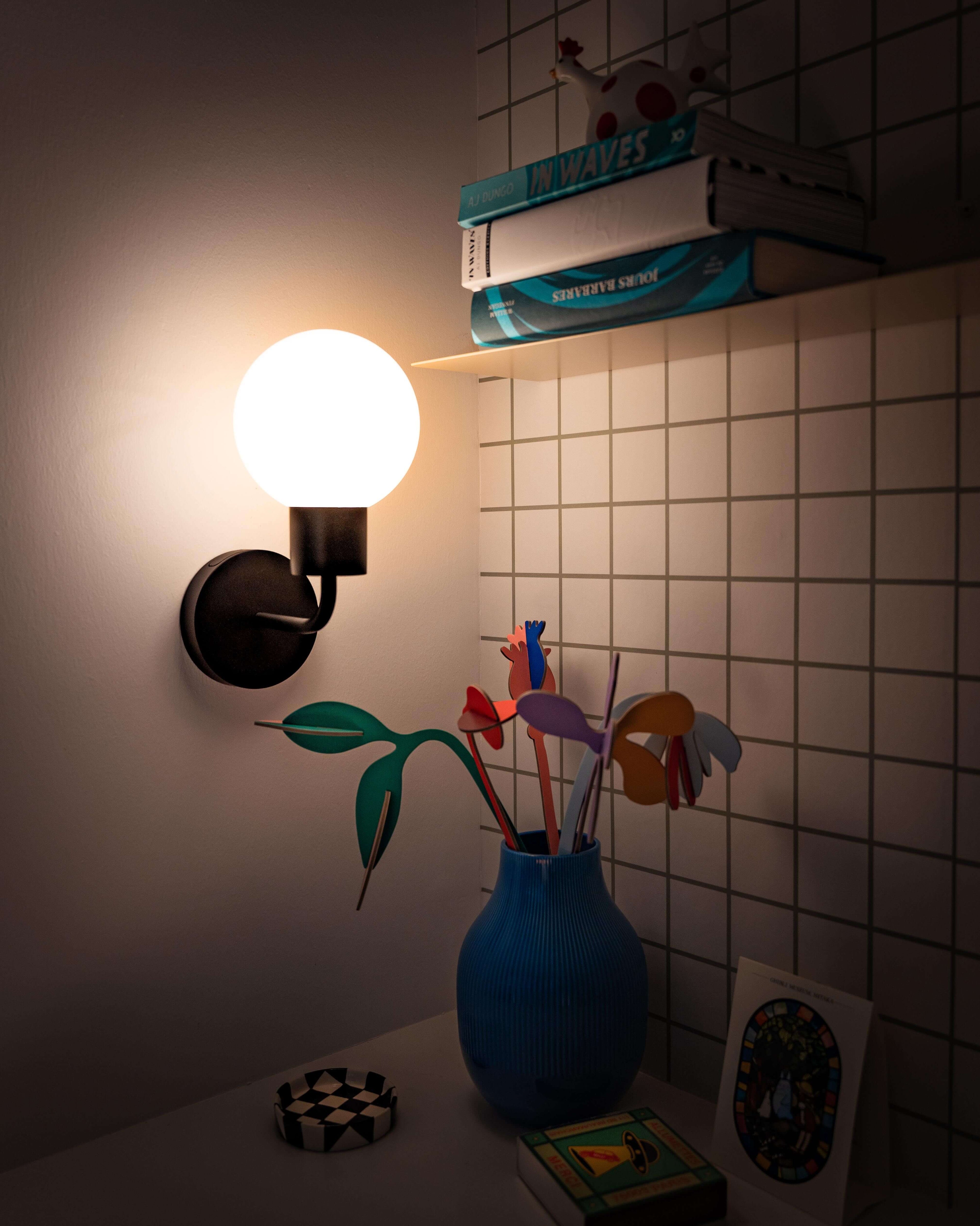 Modern rechargeable wall sconce illuminating a stylish room with vibrant decor and a blue vase on a shelf.