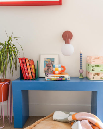 Modern interior with rechargeable wall sconce above a blue table, decorated with books, plants, and colorful decor.