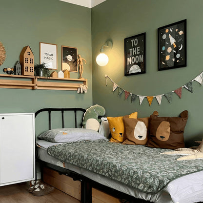Kids bedroom with wall painted in green, some decorative kid friendly art pieces and a sage green wall light sconce