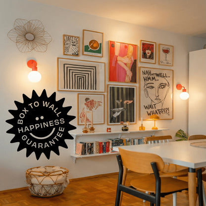 A styled interior wall with multiple framed art prints in a gallery wall arrangement, warm wall sconces, a dining table and chairs, and a large black &