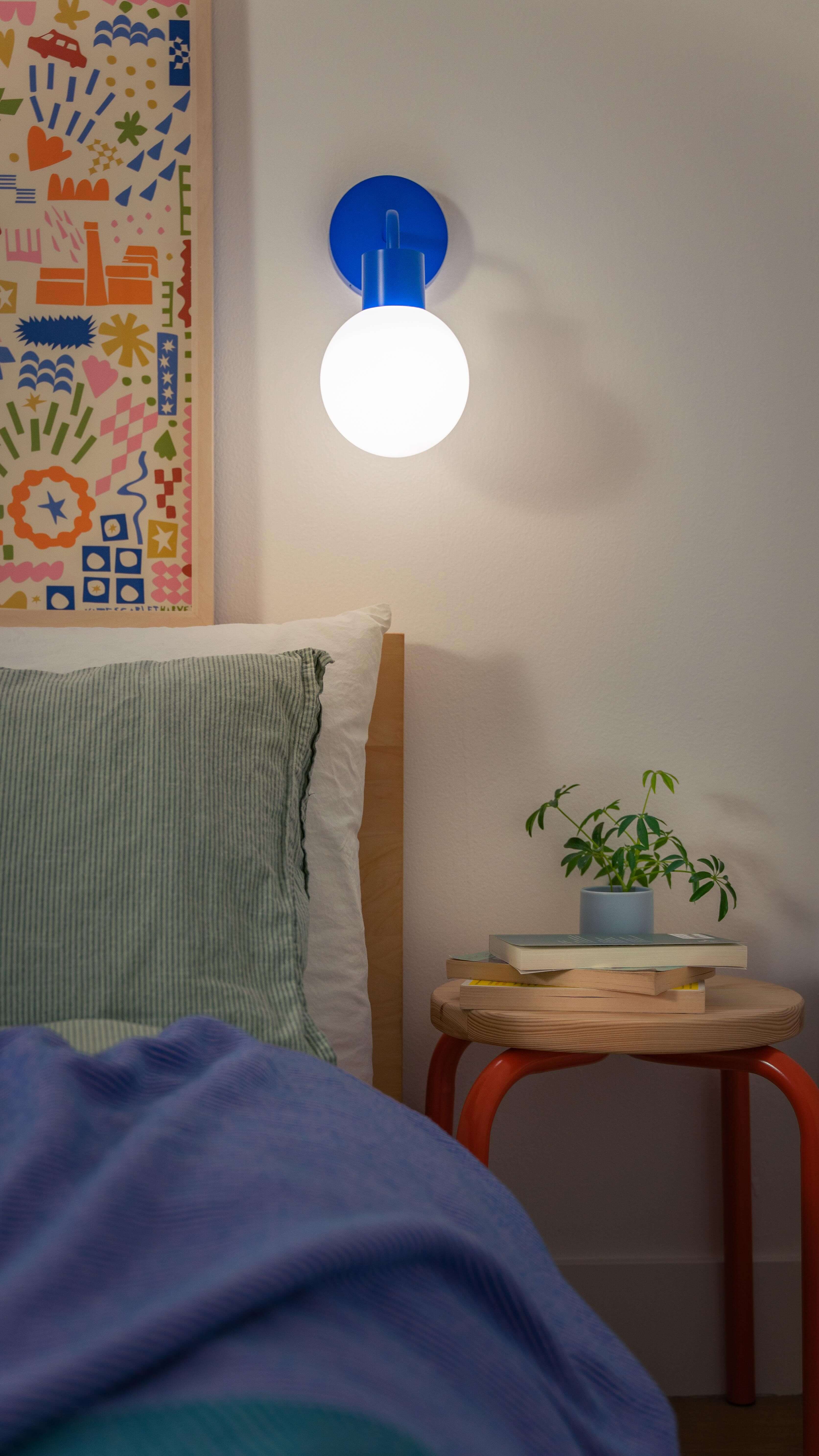 Modern bedroom with a rechargeable wall sconce, featuring a glowing bulb, colorful artwork, and cozy decor.
