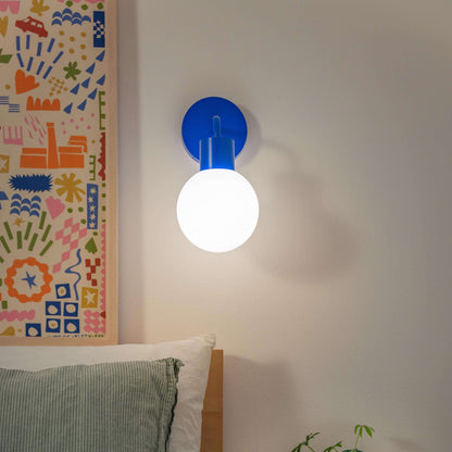 Modern bedroom with a rechargeable wall sconce, featuring a glowing bulb, colorful artwork, and cozy decor.