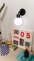 Modern rechargeable wall sconce with round bulb illuminating a stylish desktop calendar and decor setup on a white wall.